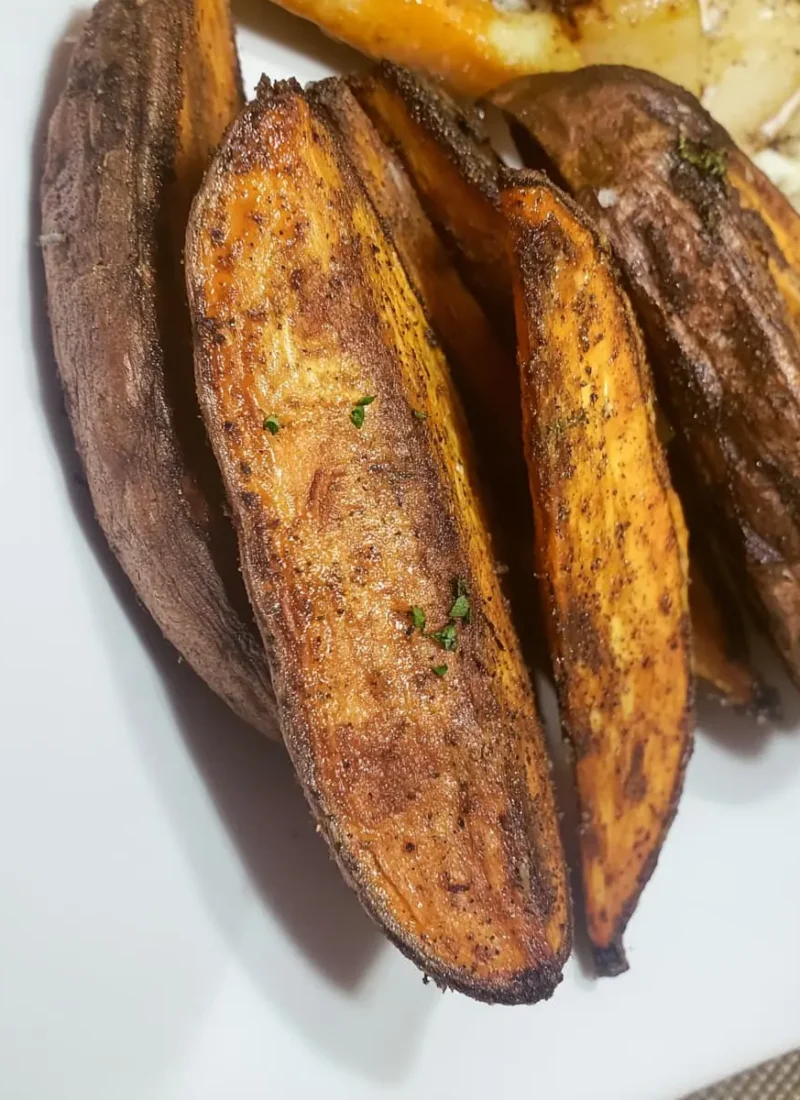 Close-up of golden, crispy potato wedges coated in spices and herbs on a white plate.