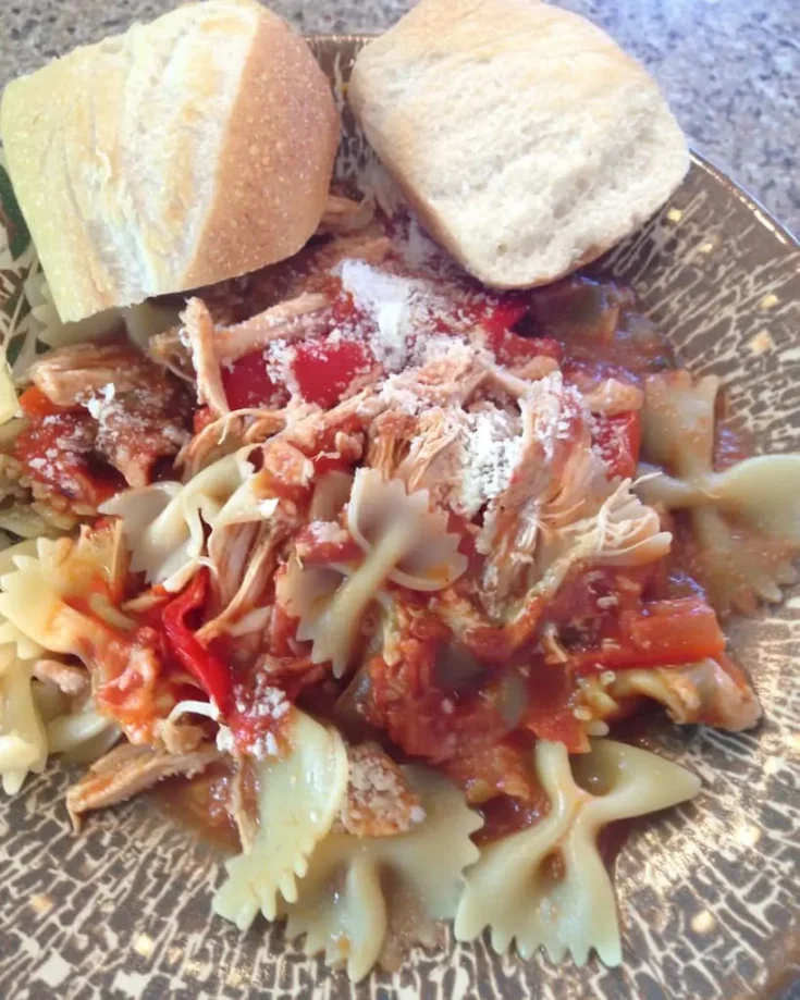 Tender shredded chicken cacciatore served over bow tie pasta with tomatoes, peppers, and onions, topped with grated Parmesan cheese and crusty Italian bread on the side