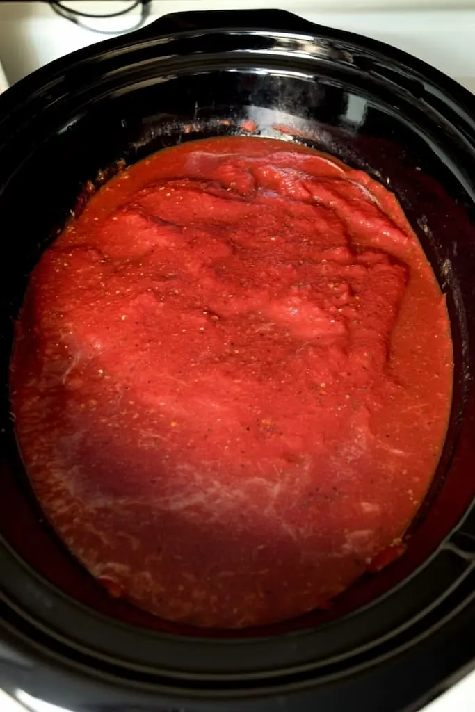 Rich red tomato sauce with herbs simmering in black slow cooker insert for chicken cacciatore recipe preparation