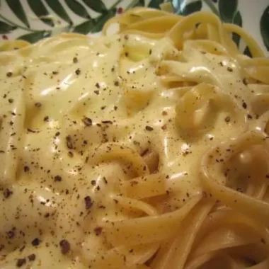 Close-up of cooked Fettuccine Alfredo topped with creamy sauce and cracked black pepper