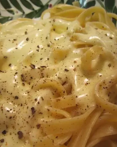 Close-up of cooked Fettuccine Alfredo topped with creamy sauce and cracked black pepper