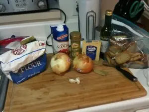 Wooden board with onions, beef stock, flour, wine, Gruyere, herbs, and toasted baguette slices for French onion soup