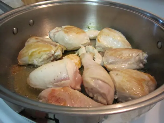 Raw chicken pieces being browned in a stainless steel skillet as the first step in making Arroz Con Pollo