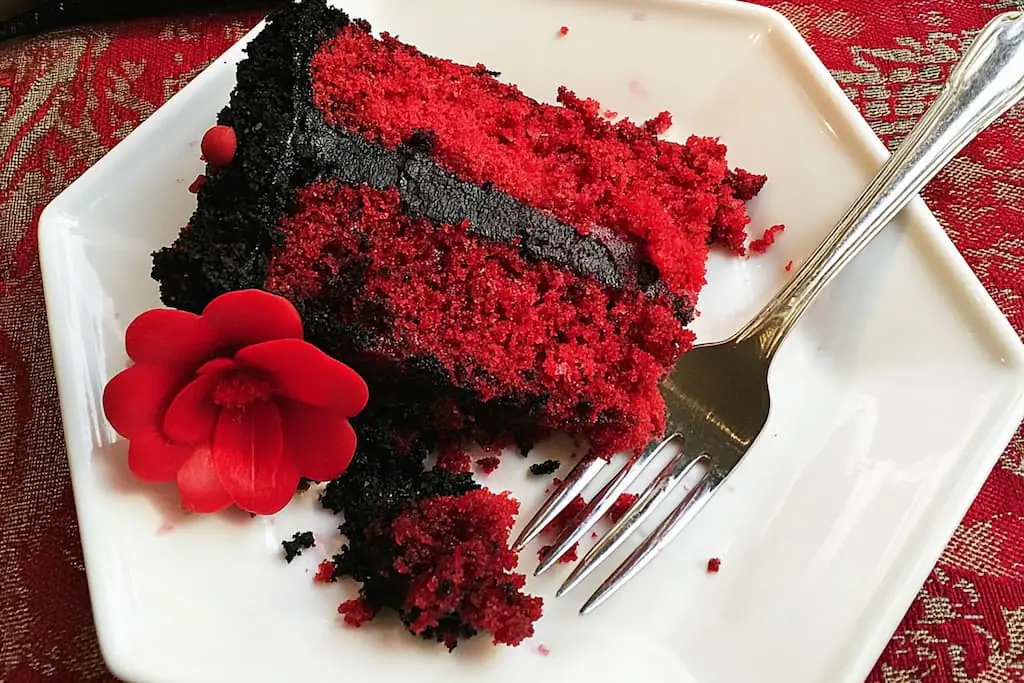 Slice of gothic Halloween cake showing bright red velvet layers with black buttercream frosting on a white plate with silver fork