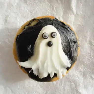 Overhead view of Halloween ghost cupcake showing white frosting shaped into ghost with candy eyes on dark chocolate icing