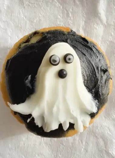 Overhead view of Halloween ghost cupcake showing white frosting shaped into ghost with candy eyes on dark chocolate icing