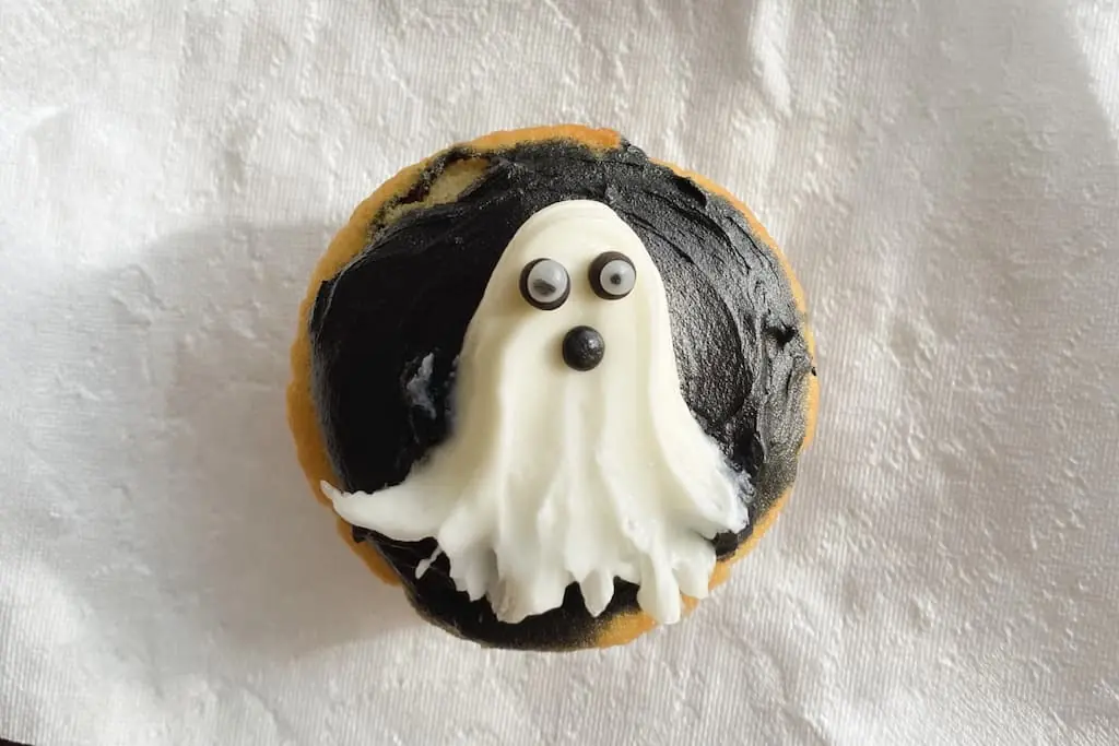 Overhead view of Halloween ghost cupcake showing white frosting shaped into ghost with candy eyes on dark chocolate icing