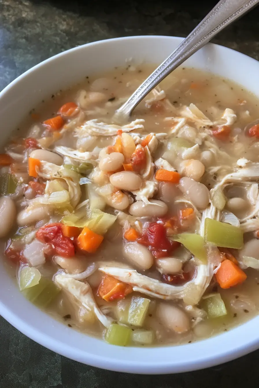 Bowl of healthy white chicken chili with shredded chicken breast, white beans, chopped carrots, celery, tomatoes, and onions in a light broth.
