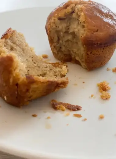 Cross-section view of a high protein banana muffin showing the tender, golden crumb structure with one half broken apart on a white plate with scattered crumbs