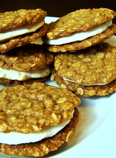 Stack of homemade oatmeal cream pies with fluffy vanilla filling between soft cinnamon oatmeal cookies on a white plate
