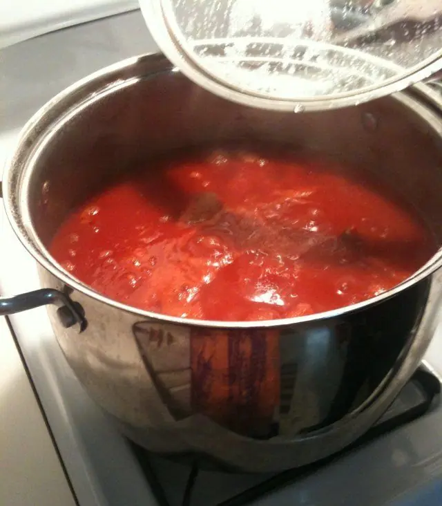 Large pot of old style Italian gravy simmering on the stove with beef and sausage cooking in rich tomato sauce.