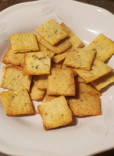 Golden-brown homemade keto crackers made with almond flour and cheddar, served on a white plate with leaf detailing.