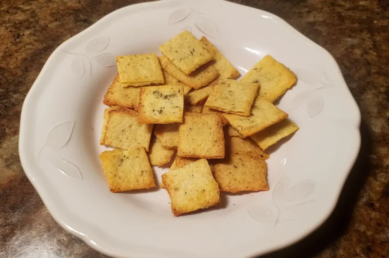 Golden-brown homemade keto crackers made with almond flour and cheddar, served on a white plate with leaf detailing.