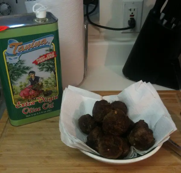 Bowl of homemade Italian meatballs resting on paper towels next to a tin of extra virgin olive oil on a kitchen counter.