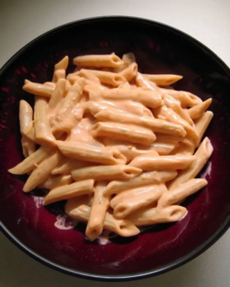 Creamy penne alla vodka pasta in a dark purple bowl, showing the silky pink vodka sauce coating ridged penne noodles perfectly