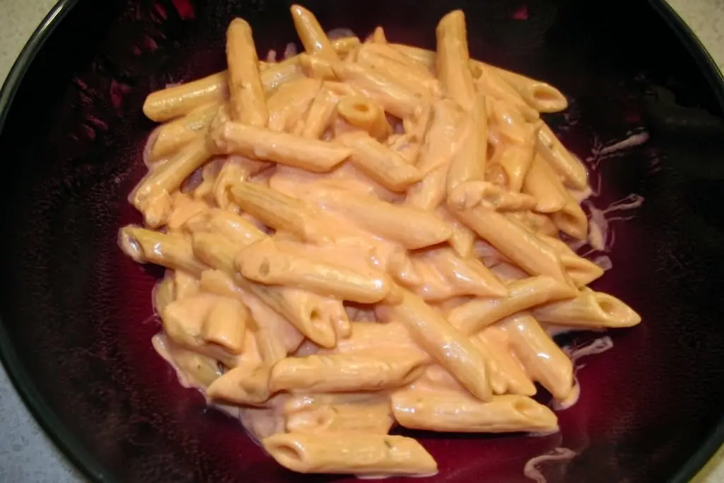 Perfectly coated penne alla vodka pasta in a dark bowl showing creamy pink sauce clinging to every ridged noodle