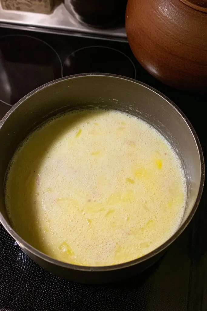 Potato leek soup simmering in heavy pot on stovetop with diced potatoes visible in pale broth