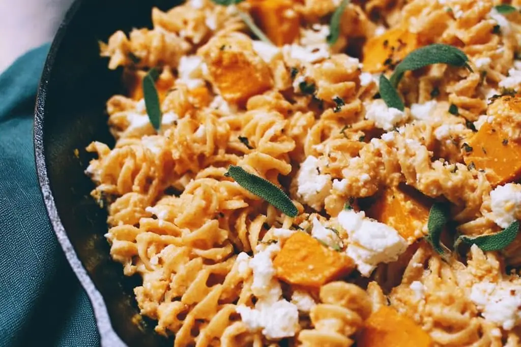 Cast-iron skillet filled with rotini tossed in creamy butternut squash sauce, topped with roasted squash cubes, crumbled feta, and fresh sage leaves.