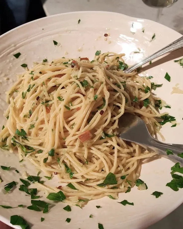 Golden spaghetti with garlic and oil garnished with fresh parsley on white ceramic plate, showing perfectly coated pasta strands glistening with olive oil