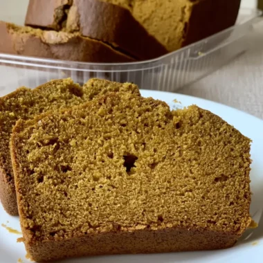 Sliced, moist pumpkin bread loaf inspired by the Starbucks pumpkin bread recipe sitting on a white plate, with the remaining loaf in a clear container behind it.