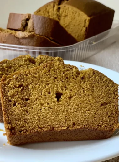 Sliced, moist pumpkin bread loaf inspired by the Starbucks pumpkin bread recipe sitting on a white plate, with the remaining loaf in a clear container behind it.