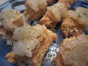 Unbaked chicken breasts rolled with shredded cheese, coated in breadcrumbs, and topped with raw shrimp and dried herbs in a glass baking dish