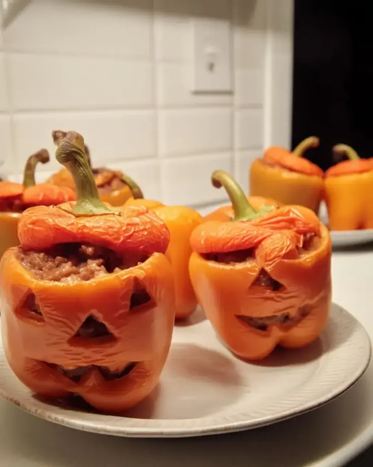 Carved orange bell peppers with jack-o'-lantern faces filled with seasoned ground beef on white plates in a bright kitchen
