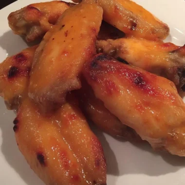 rispy sweet-and-spicy chicken wings glazed with Thai sweet-chili sauce, stacked on a white plate.