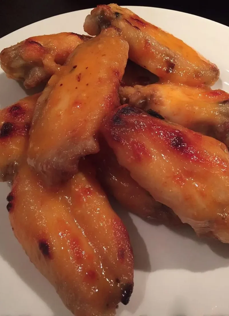 rispy sweet-and-spicy chicken wings glazed with Thai sweet-chili sauce, stacked on a white plate.