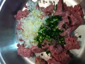 Raw ground turkey in a pan with chopped onions, garlic, and jalapeños during the first step of turkey chili preparation