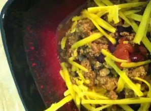 Hearty bowl of spicy turkey chili topped with shredded cheddar cheese, served in a black and red dish