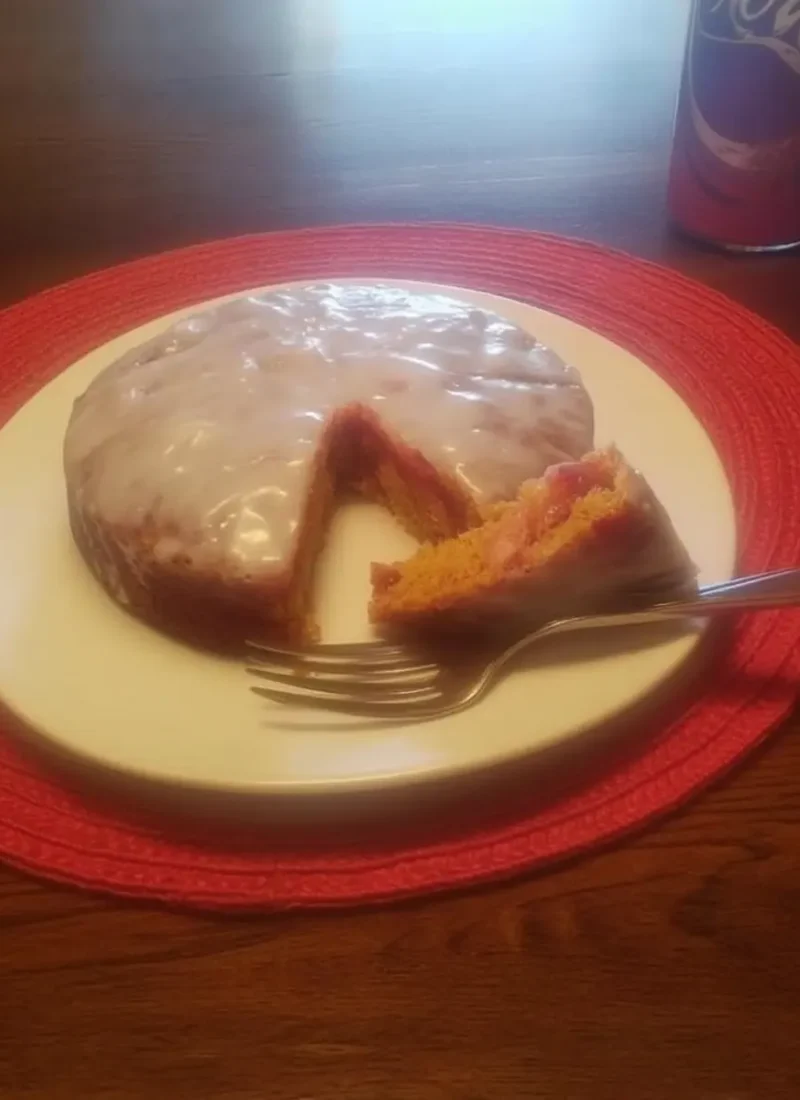A slice of white chocolate raspberry poke cake on a plate, showing moist layers with raspberry filling and a glossy white icing on top.