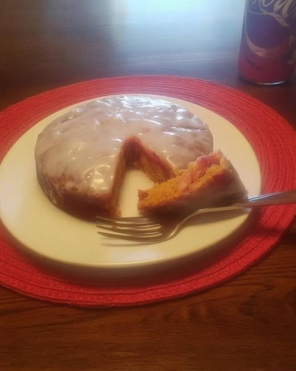 A slice of white chocolate raspberry poke cake on a plate, showing moist layers with raspberry filling and a glossy white icing on top.