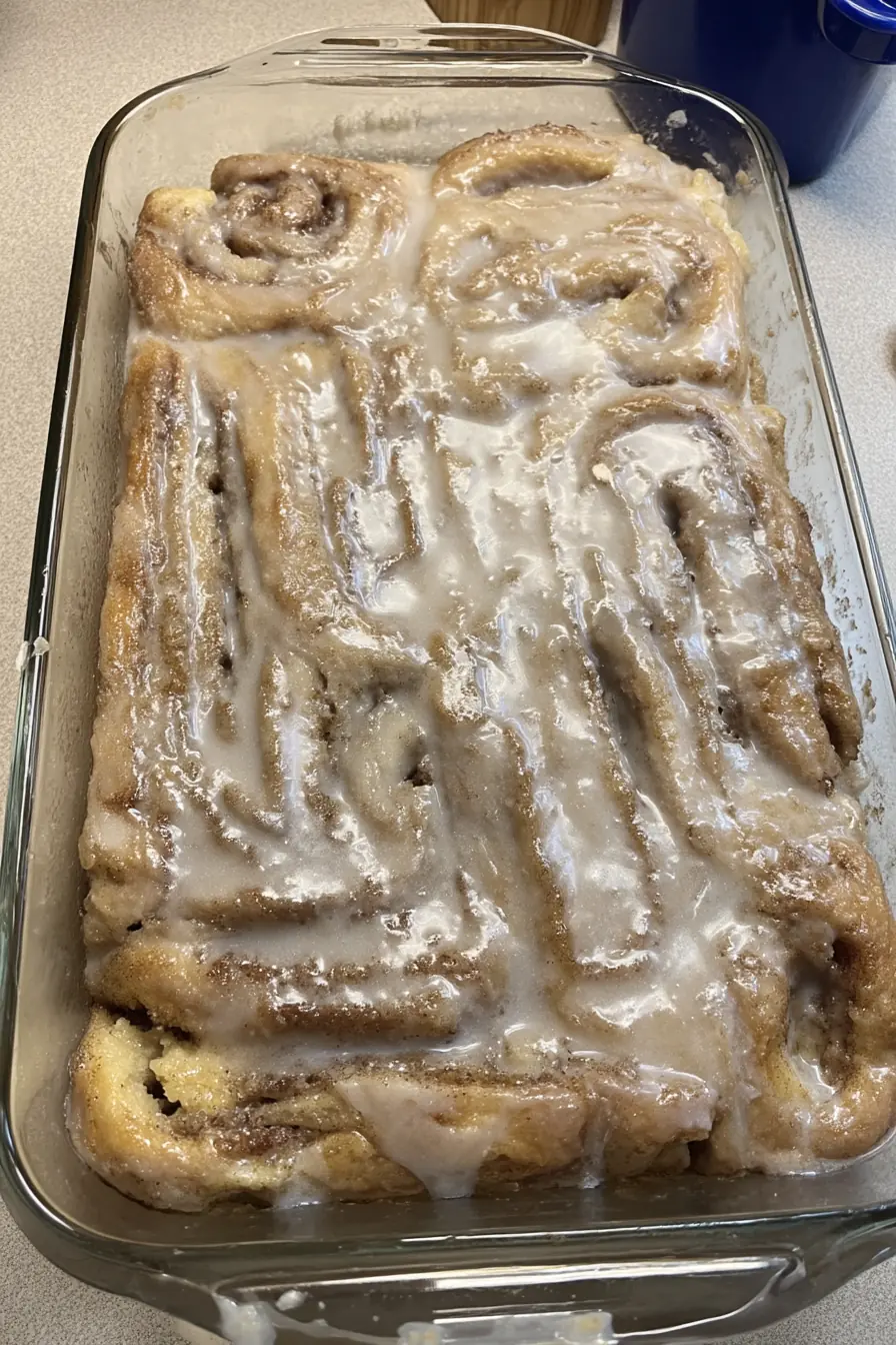 Freshly baked cinnamon roll cake in a glass dish, topped with a thick vanilla glaze and cinnamon swirls.